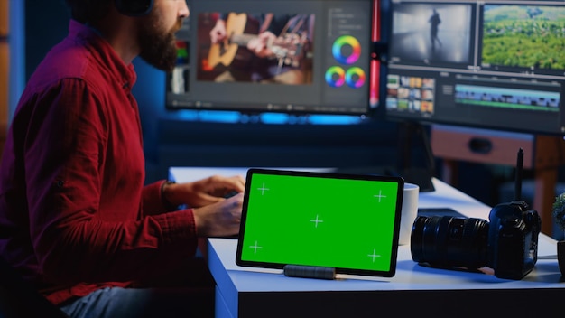 Foto gratuita tablet con schermo verde sulla scrivania di un'agenzia multimediale accanto all'editore video che lavora per una società di produzione