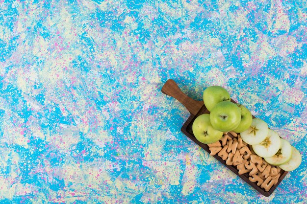 Зеленые нарезанные яблоки с крекерами на деревянной доске, вид сверху