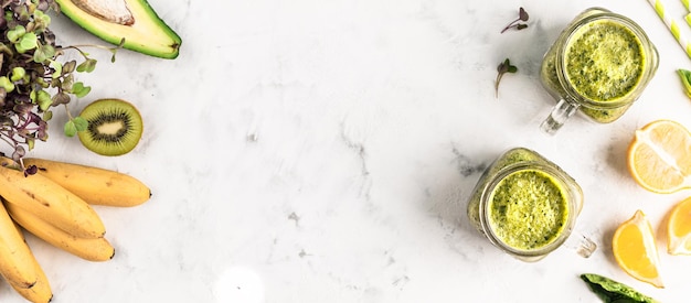 Green smoothie of vegetables and fruits with ingredients in glass jars on a white background, top view, copy space. banner