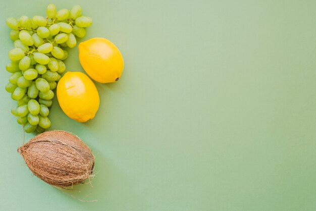 Зеленая поверхность с лимонами, кокосом и гроздью винограда