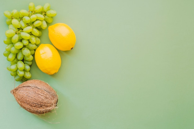 Green surface with lemons, coconut and bunch of grapes