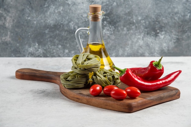 Green tagliatelle, vegetables and olive oil on wooden board.