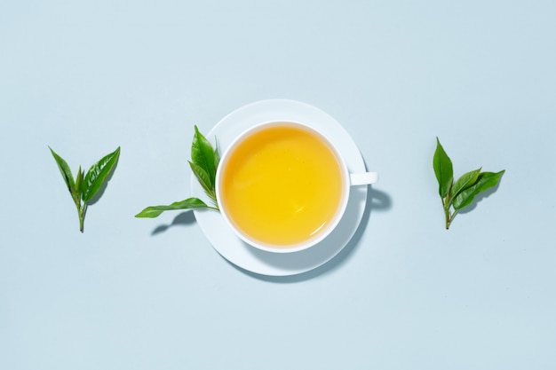 Зеленый чай, сваренный в чашке с чайными листьями на синем пастельном фоне. Вид сверху.