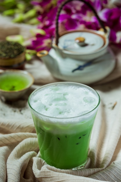 Green tea iced in a tall glass with cream topped with iced green tea. Decorated with green tea powder.