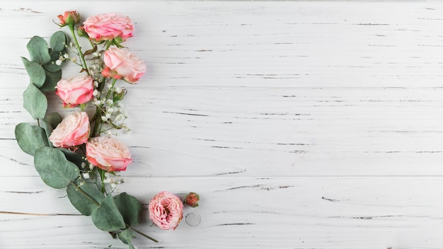 Зеленая веточка; розовые розы и белая гипсофила на белом фоне деревянные текстурированные