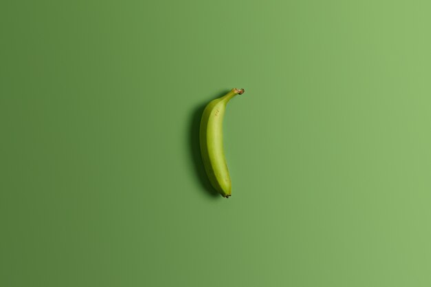 Green unripe whole banana on bright studio background. Tasty appetizing tropical fruit. Clean eating, healthy nutritious and dietary snack. Top view and flat lay. Horizontal shot. Food concept