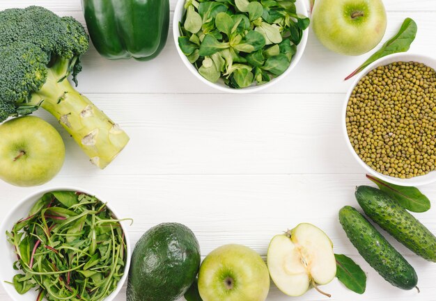 Green vegetables arranged in circular shape on white plank board