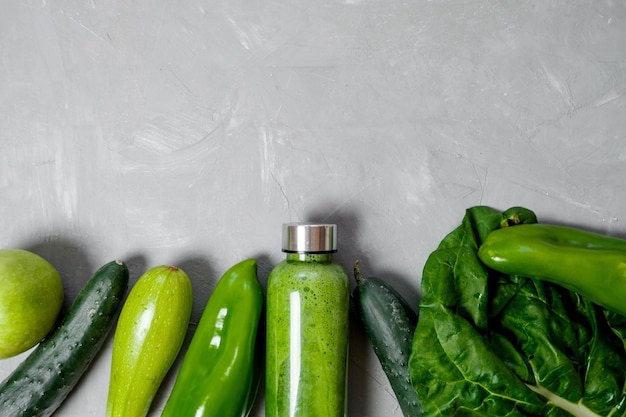 Зеленые овощи и коктейли в пластиковой бутылке на сером фоне Здоровая концепция Вид сверху Место для текста