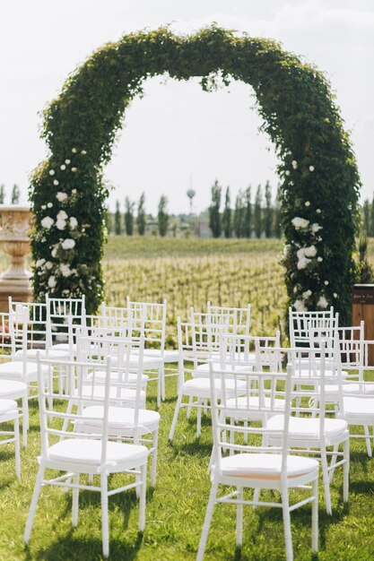 Зеленая арка свадебной церемонии и белые стулья