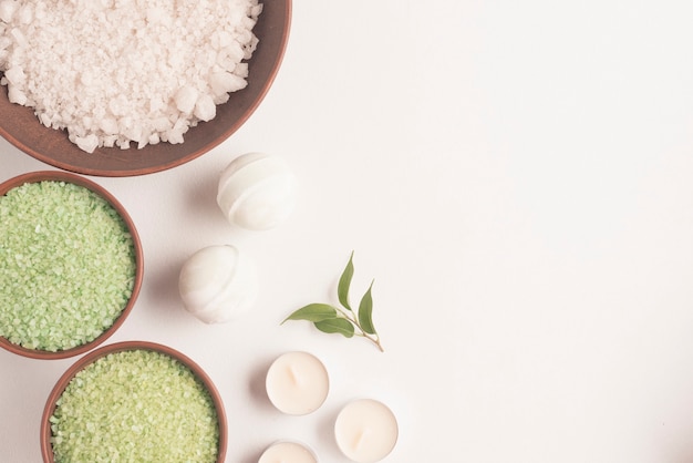 Green and white herbal sea salt with spa bomb and candles on white background