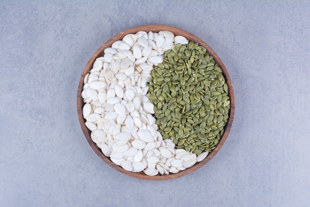 Зеленые и белые семена тыквы на деревянной тарелке на мраморе.
