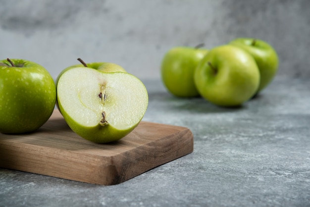 Green whole and sliced apples on wooden board.
