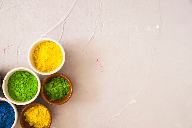 Green; yellow and blue color powder in the bowl on concrete backdrop