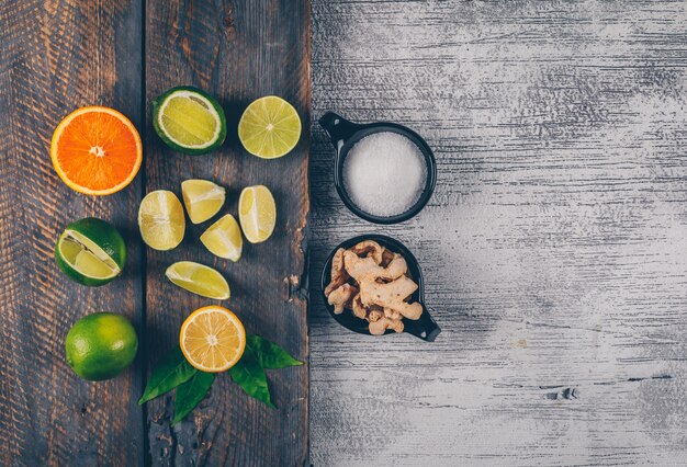 green and yellow lemons and orange with cups of salt and ginger top view on a wooden tray and gray wooden background