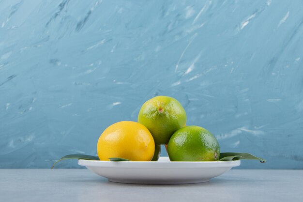 Green and yellow lemons on white plate