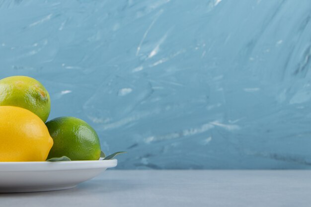 Green and yellow lemons on white plate