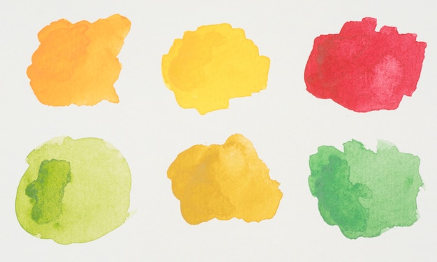 白い紙の塗料の緑色、黄色、オレンジ色、赤色のブロット