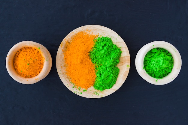 Green and yellow powder in wooden bowl and plate on black backdrop