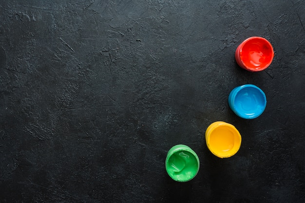 Free photo green; yellow; red and blue small paint container on slate surface