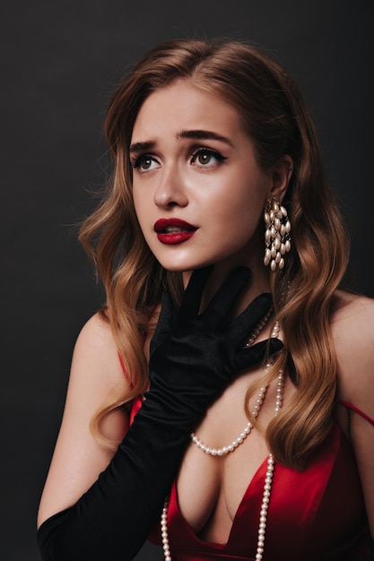 Greeneyed woman with beautiful makeup sensitively posing on black background Curly lady in red silk top emotionally posing on isolated backdrop