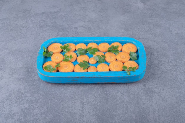 Greens and sliced carrot on the wooden tray , on the marble surface.