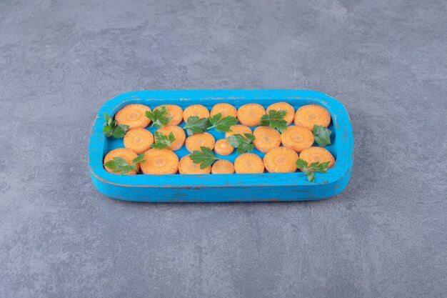 Greens and sliced carrot on the wooden tray , on the marble surface.