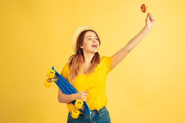 Greeting, calling. Caucasian woman's portrait on yellow studio background. Beautiful female model in hat. Concept of human emotions, facial expression, sales, ad. Summertime, travel, resort.