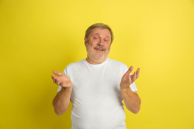 Greeting, inviting gesture. Caucasian man portrait isolated on yellow studio background. Beautiful male model in white shirt posing.