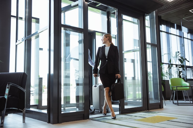Greeting. Meeting of young business partners after arriving to end point of business trip. Man and woman walking against glass wall background of modern building. Concept of business, finance, ad.