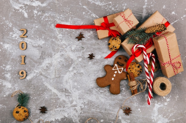 Grey brown present boxes with red ribbons stand on the floor with chocolate cookies, ginger breads and rope  before number 2019