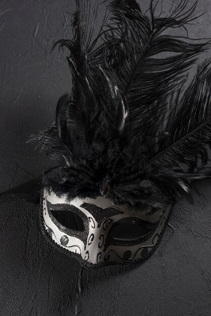 Серая карнавальная маска с пером на столе