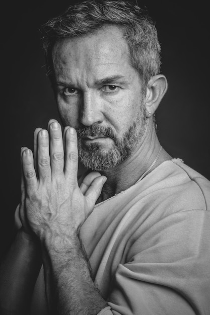 Grey haired mature man put hands together looking at camera Handsome middle aged man in black and white photo Black and white portrait of attractive beautiful serious man