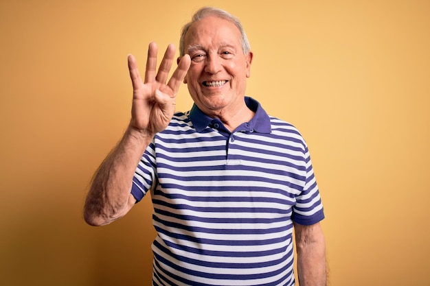Grey haired senior man wearing casual navy striped tshirt standing over yellow background showing and pointing up with fingers number four while smiling confident and happy