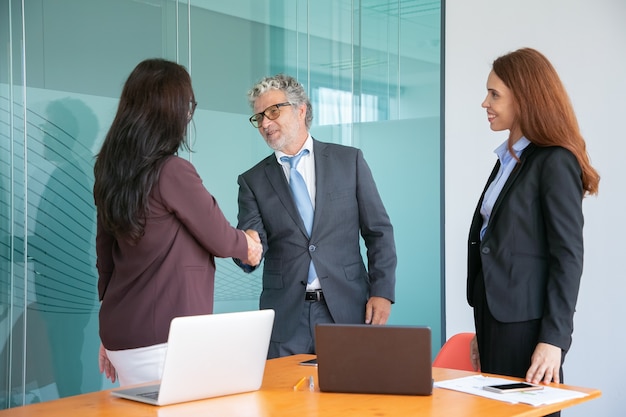 Grey-haired senior manager handshaking and greeting businesswoman