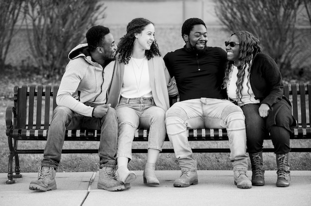 Free photo grey scale shot of a group of friends happily sitting on a bench