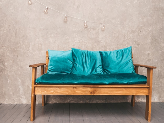 Интерьер серой стены со стильным обитым синим и деревянным современным диваном, подвесными светильниками
