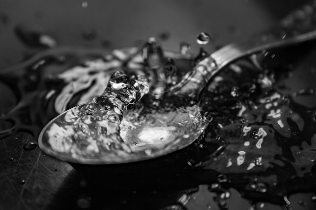 Greyscale closeup of water droplets on a spoon on a table against a blurry background
