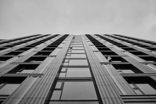 Greyscale of a modern skyscraper under the cloudy sky