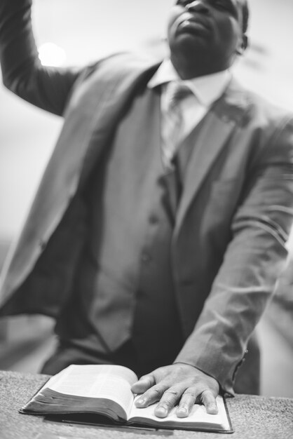 Greyscale shot of an African-American male praying with his hand on the Bible