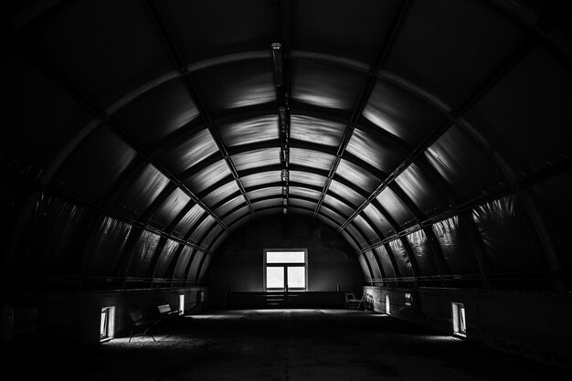 Greyscale shot of a dark tunnel room with a window