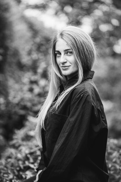 Greyscale shot of a fashionable caucasian blonde female posing surrounded by greenery