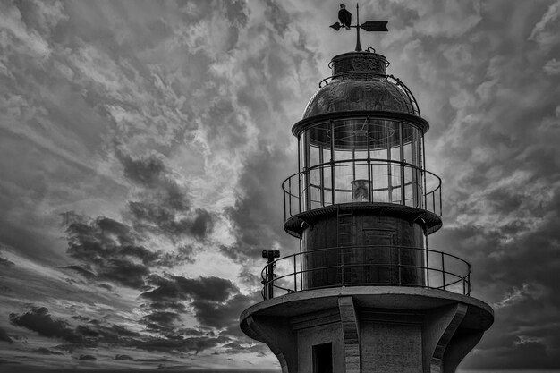 Greyscale shot of a lighthouse with an eagle on its top