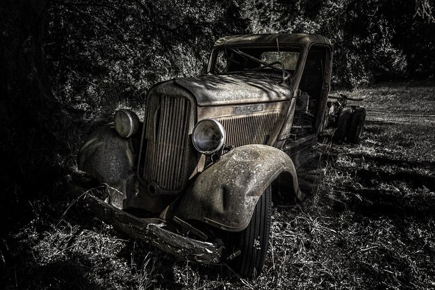 Greyscale shot of an old retro car in the forest during daytime