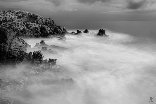 Greyscale shot of the rocks on the body of the foamy sea