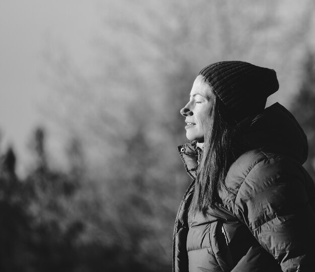 Greyscale of the side profile of a woman with a beanie surrounded by trees