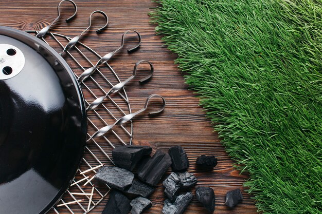 Grill grates with metallic skewer and coal on wooden textured