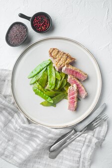 구운 ahi tuna steak 세트, 봄 양파와 설탕 스냅 완두콩, 접시, 하얀 돌 배경, 평면도