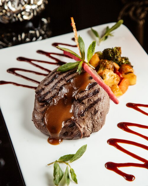 grilled beef fillet medallion with sauce and vegetables on a white plate