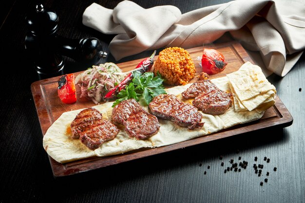 Филе говядины на гриле с булгуром и овощами на деревянной доске. турецкий кебаб. крупным планом, выборочный фокус
