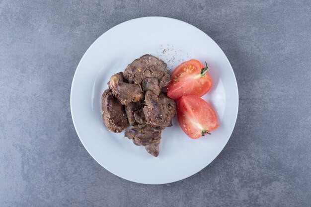 Grilled beef kebab and tomato on white plate.